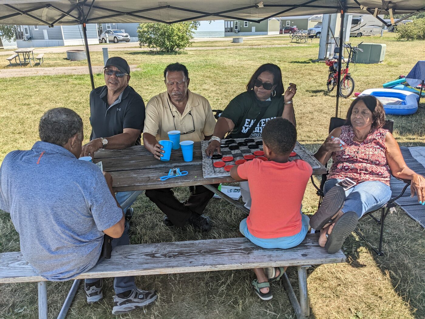 Family playing giant checkers under the canopy at the campground